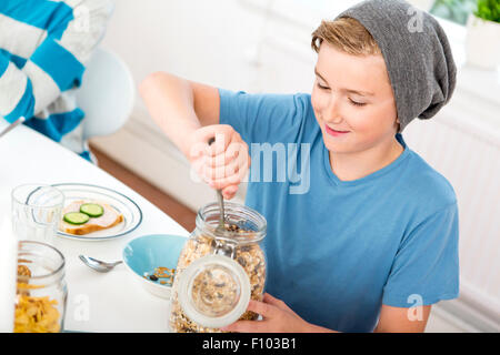 Teenage boy serving cereals out of a bottle at the breakfast table. Stock Photo