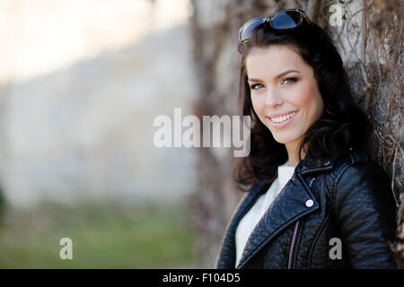 Portrait of a smiling, beautiful young woman leaning against a wall Stock Photo
