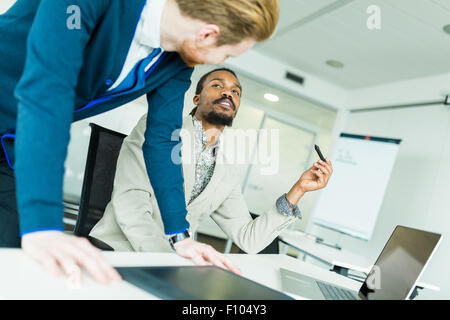 A black young man with dreadlocks and a young handsome red haired businessman discussing graphics design flaws Stock Photo