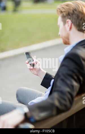 Businessman holding his cell phone while sitting on a park bench Stock Photo