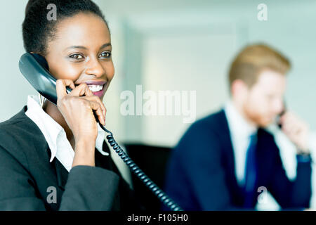 A beautiful, black, young woman working at a call center in an office with her red haird partner on the other end of the desk ta Stock Photo