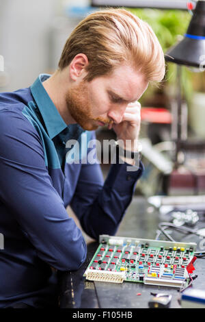 Young handsome man thinking while soldering a circuit board and working on fixing hardware Stock Photo