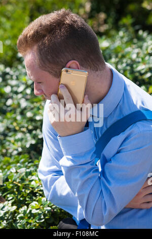 Young man wearing blue shirt using gold iphone with Apple logo at Bournemouth, Dorset UK in August Stock Photo