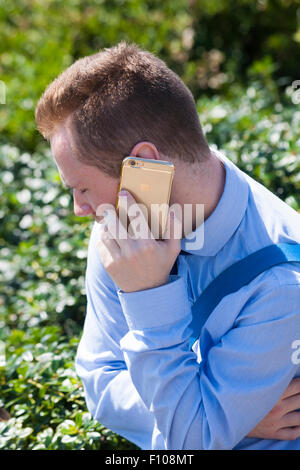 Young man wearing blue shirt using gold iphone with Apple logo at Bournemouth, Dorset UK in August Stock Photo