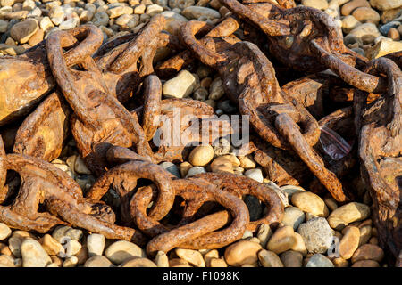 Old rusty ship chain lying on a rocky beach Stock Photo
