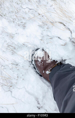 A person wearing walking boots in Winter. Looking down on a hiking boot being used in snow, England, UK Stock Photo