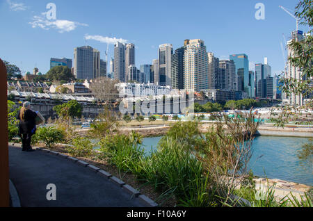 Sydney August 2015: A woman looks back over Nawi Cove towards Sydney CBD from Barangaroo Headland Reserve on the shores of Sydney Harbour Stock Photo