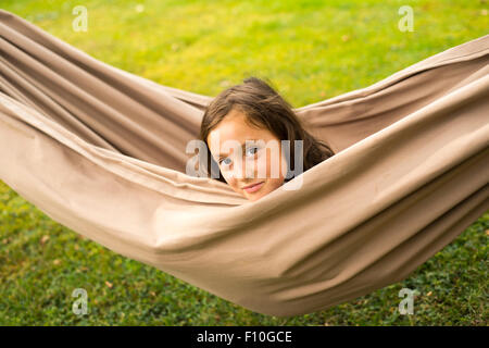 Portrait of young child brunette girl in hammock, outdoors, summertime, looking at camera, backyard, garden, head Stock Photo