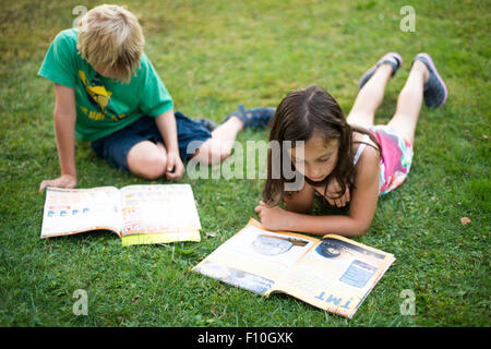 Kids reading together enjoying and reading a magazine laying on the grass outdoors Stock Photo