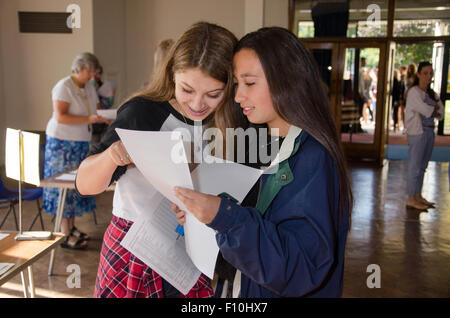 Two teenage girls standing together in their school hall looking pleased with their GCSE exam results. Stock Photo