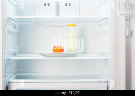 Two-colored orange and red peach on white plate and a glass bottle of yogurt in open empty refrigerator. Weight loss diet concep Stock Photo