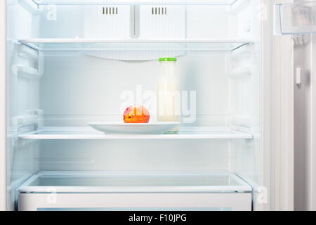 Two-colored orange and red peach on white plate and a glass bottle of yogurt in open empty refrigerator. Weight loss diet concep Stock Photo