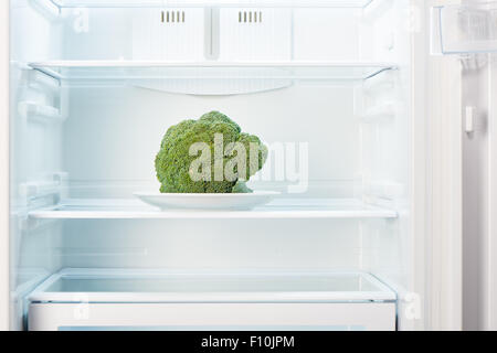 Green broccoli on white plate in open empty refrigerator. Weight loss diet concept. Stock Photo