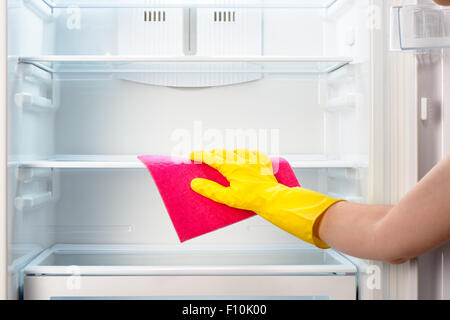 Woman's hand in yellow rubber protective glove cleaning white open empty refrigerator with pink rag Stock Photo
