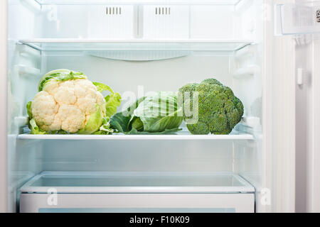 Cauliflower, green cabbage and green broccoli on shelf of open empty refrigerator. Weight loss diet concept. Stock Photo