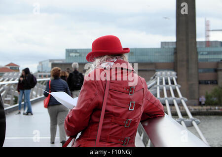 Rear view of tourist in red coat & bowler hat looking at map on the Millennium Bridge with view of Tate London UK  KATHY DEWITT Stock Photo