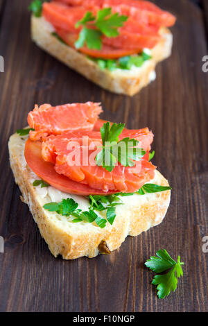 Sandwich with salmon (trout), cream cheese, tomato and parsley on rustic wooden background close up Stock Photo