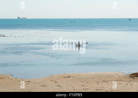 A person rowing a small boat on the sea shore at low tide at Bembridge Isle of Wight UK Stock Photo