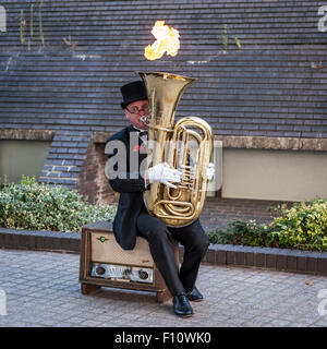 London, UK. 22 August 2015.  A street entertainer on the South Bank entertains passers by as he plays a tuba which blows flames  Stock Photo