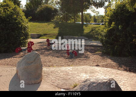 Three free seats, three red rocking horses with coil sprin at a public city park north of Indianapolis, centered, lots of shadow Stock Photo