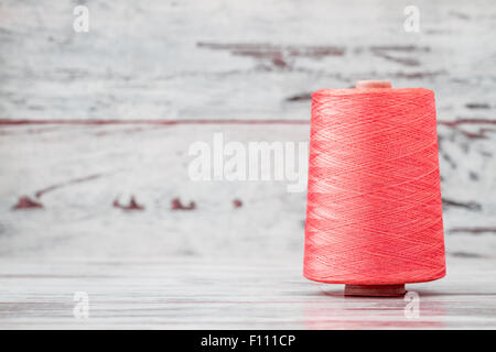 Spool of synthetic pink thread on white wooden background Stock Photo