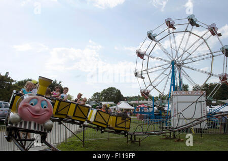 Children ride a kiddy ride at county fair with ferris wheel in background Stock Photo