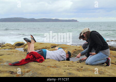 Three young ladies exploring the sea life ecology in a tidal rock pool on Pearl Beach, New South Wales, NSW, Australia. Stock Photo