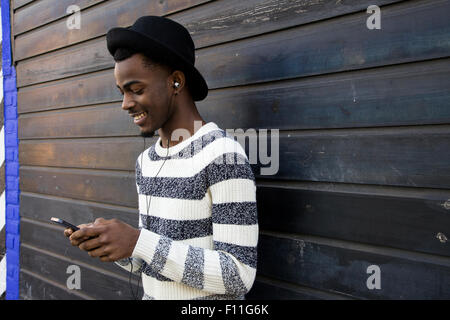 Black man listening to mp3 player near wooden wall Stock Photo