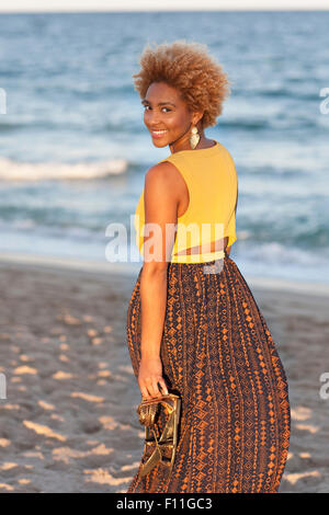 Black woman carrying sandals on beach Stock Photo