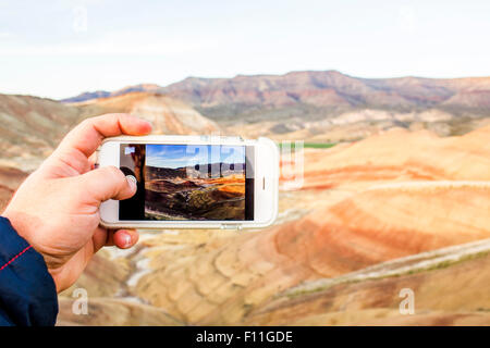 Caucasian man taking cell phone photograph of desert landscape, Painted Hills, Oregon, United States Stock Photo