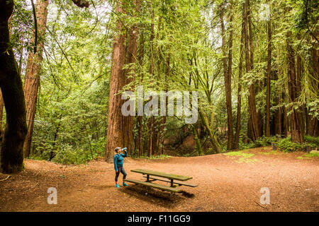 Caucasian woman drinking from bottle in forest clearing Stock Photo