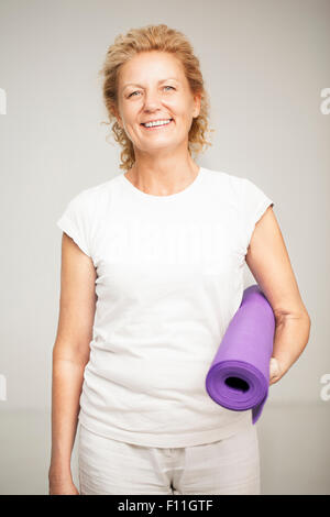 Smiling woman holding exercise mat Stock Photo