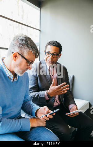 Businessmen using cell phones in office lobby Stock Photo