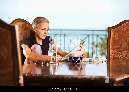 Hispanic woman reading newspaper at table Stock Photo