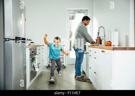 Boy skateboarding near father in kitchen Stock Photo