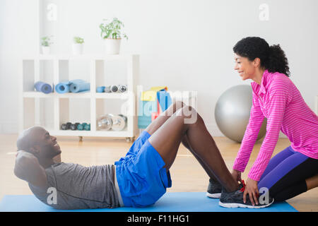Man doing sit-ups with trainer in gym Stock Photo