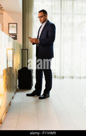 Hispanic businessman using cell phone at hotel front desk Stock Photo