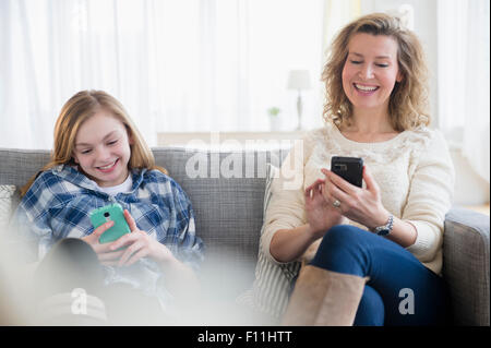 Caucasian mother and daughter using cell phones on sofa Stock Photo