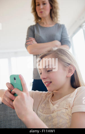 Caucasian mother watching daughter use cell phone Stock Photo