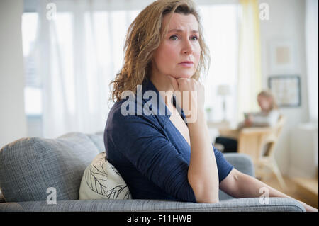Concerned Caucasian woman sitting on sofa Stock Photo