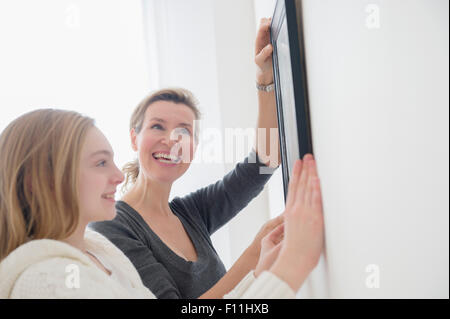 Caucasian mother and daughter hanging picture on wall Stock Photo