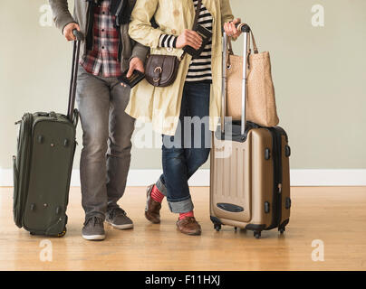 Couple holding rolling luggage in living room Stock Photo