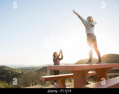 Caucasian woman photographing friend on hilltop Stock Photo