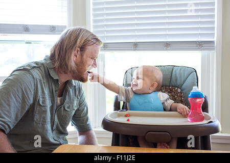Caucasian father feeding son in high chair Stock Photo