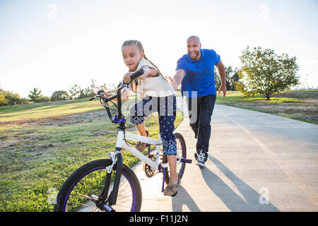 Father teaching daughter to ride bicycle in park Stock Photo