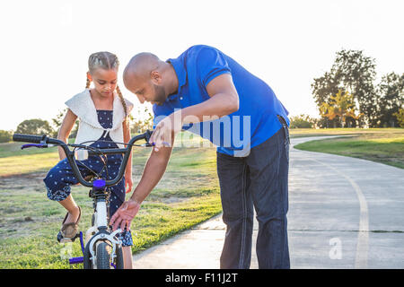 Father teaching daughter to ride bicycle in park Stock Photo