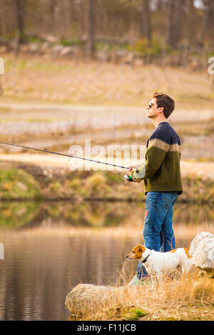 Caucasian man fishing with dog in remote lake Stock Photo