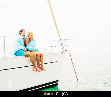 Couple wrapped in towels on deck of sailboat Stock Photo