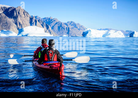 People paddling canoe towards glaciers in remote river Stock Photo