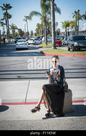Caucasian woman sitting on concrete barrier in parking lot Stock Photo